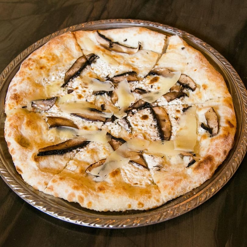 A white pizza with mushrooms and shaved cheese on a silver platter.